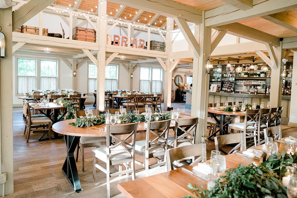Rustic, elegant banquet hall with wooden tables and greenery centerpieces.