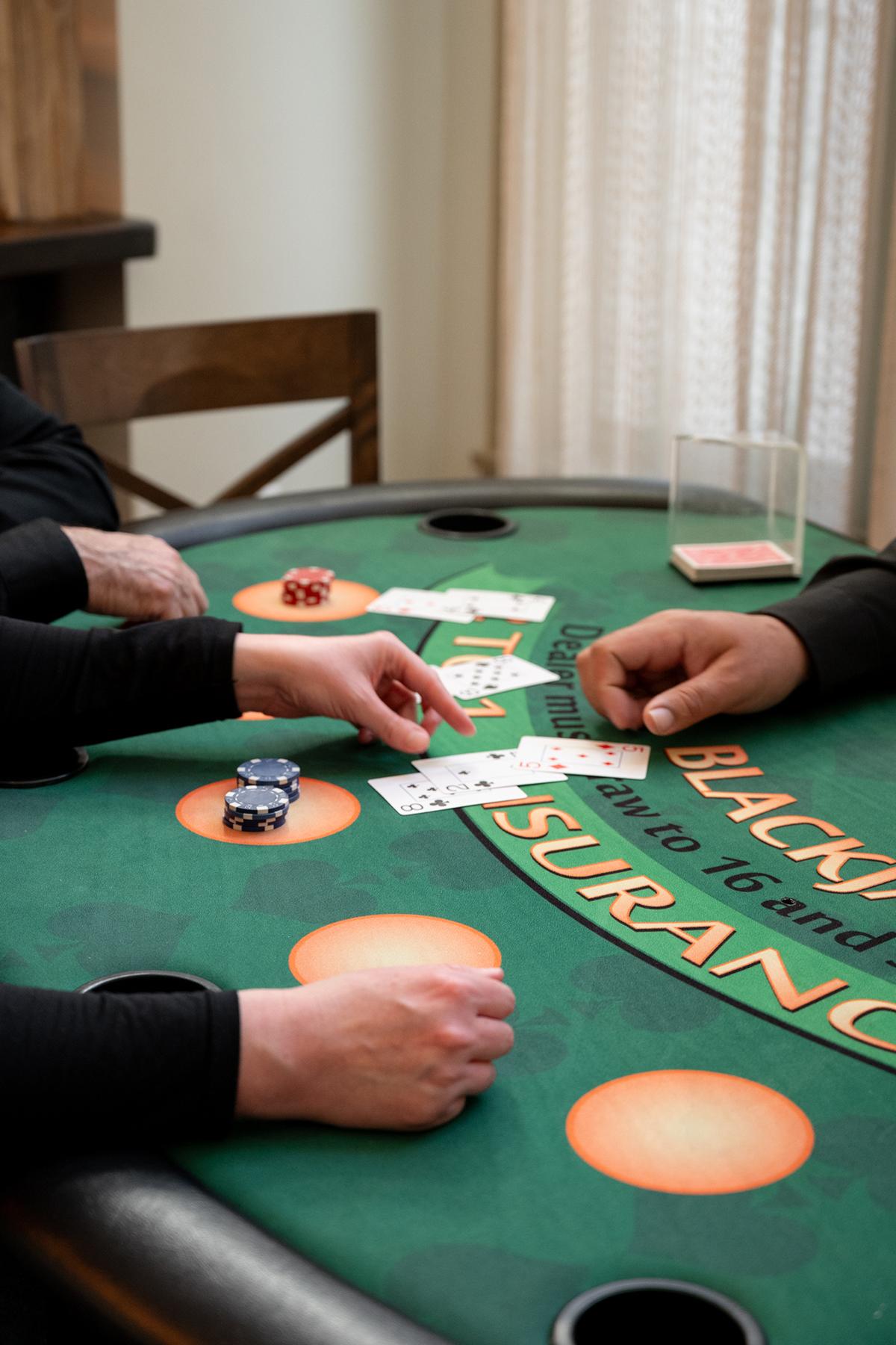 Casino table with players' hands and cards, poker chips stacked nearby.