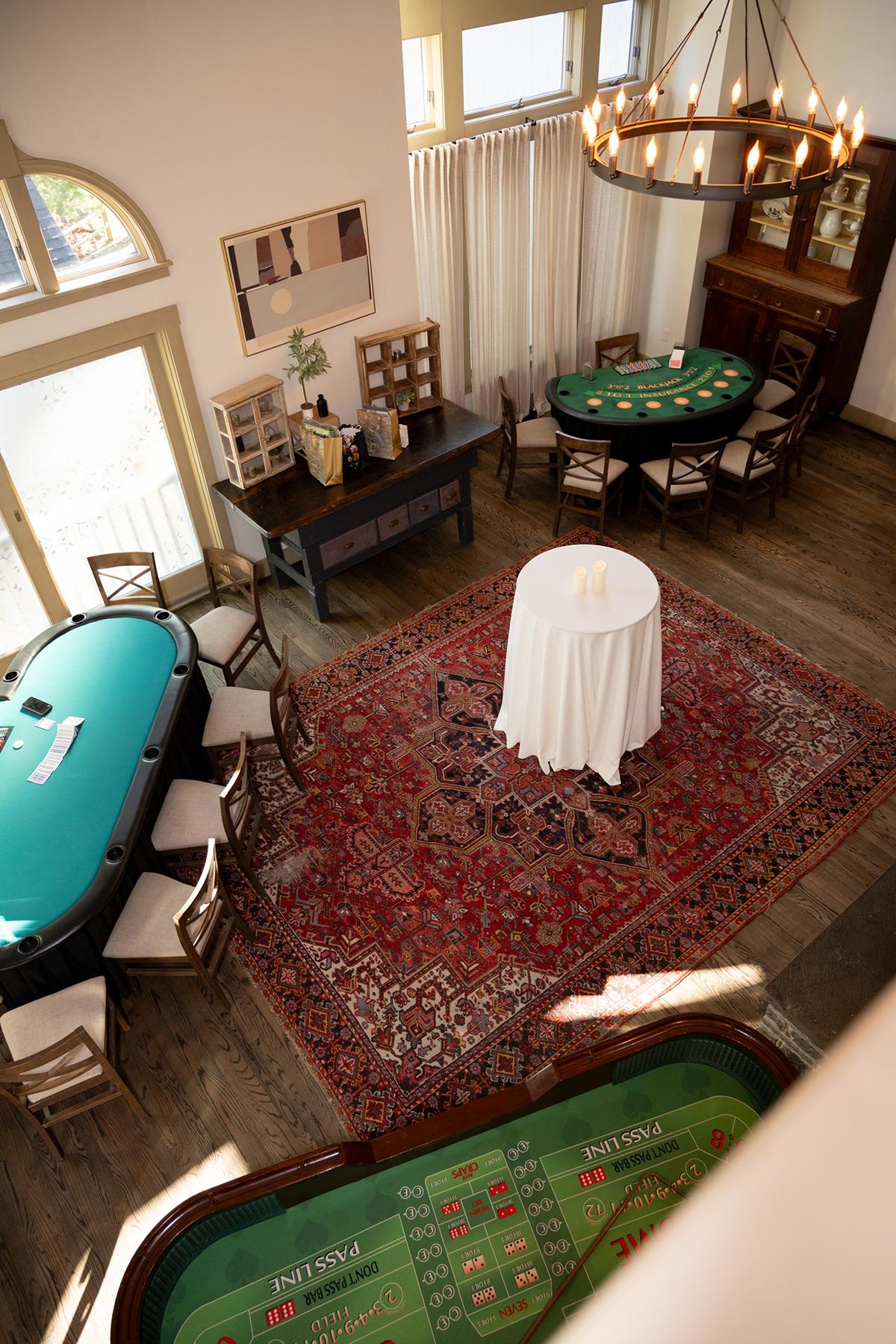 Elegant room with poker and roulette tables, chandelier, and a red patterned rug.