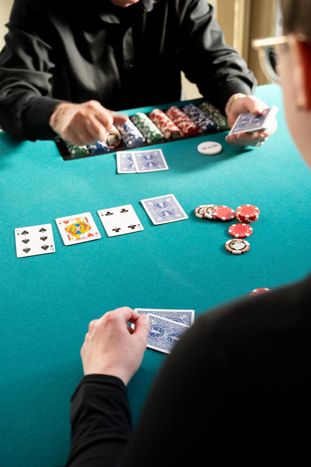 Poker game on green table, players holding cards and chips scattered around.