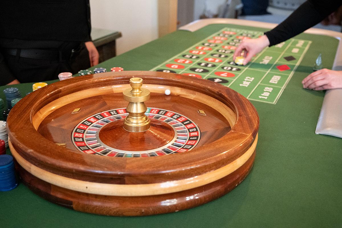 Roulette wheel and betting table with hands placing chips.