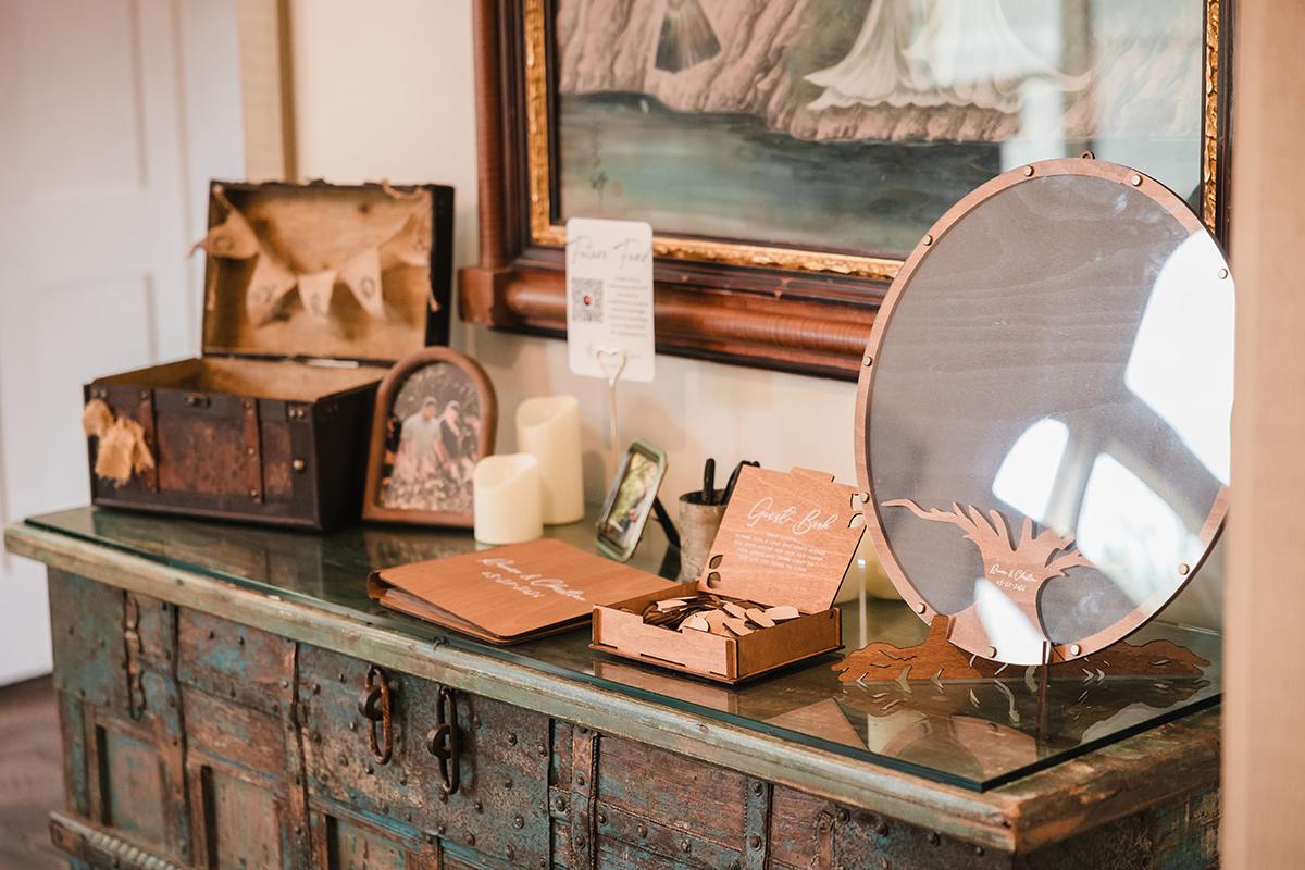 Rustic wedding decor on a wooden table, including a suitcase, candles, and a circular mirror.