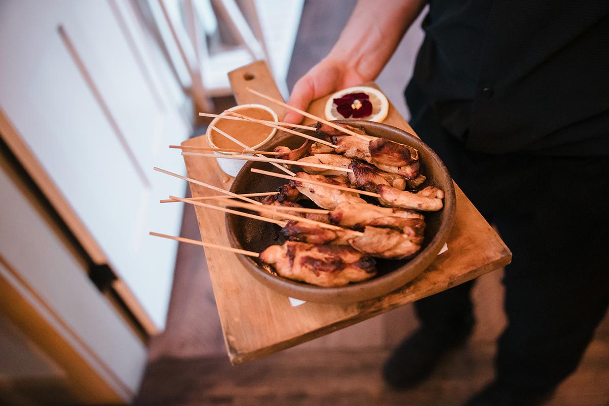 Grilled skewers on wooden board with dipping sauce.
