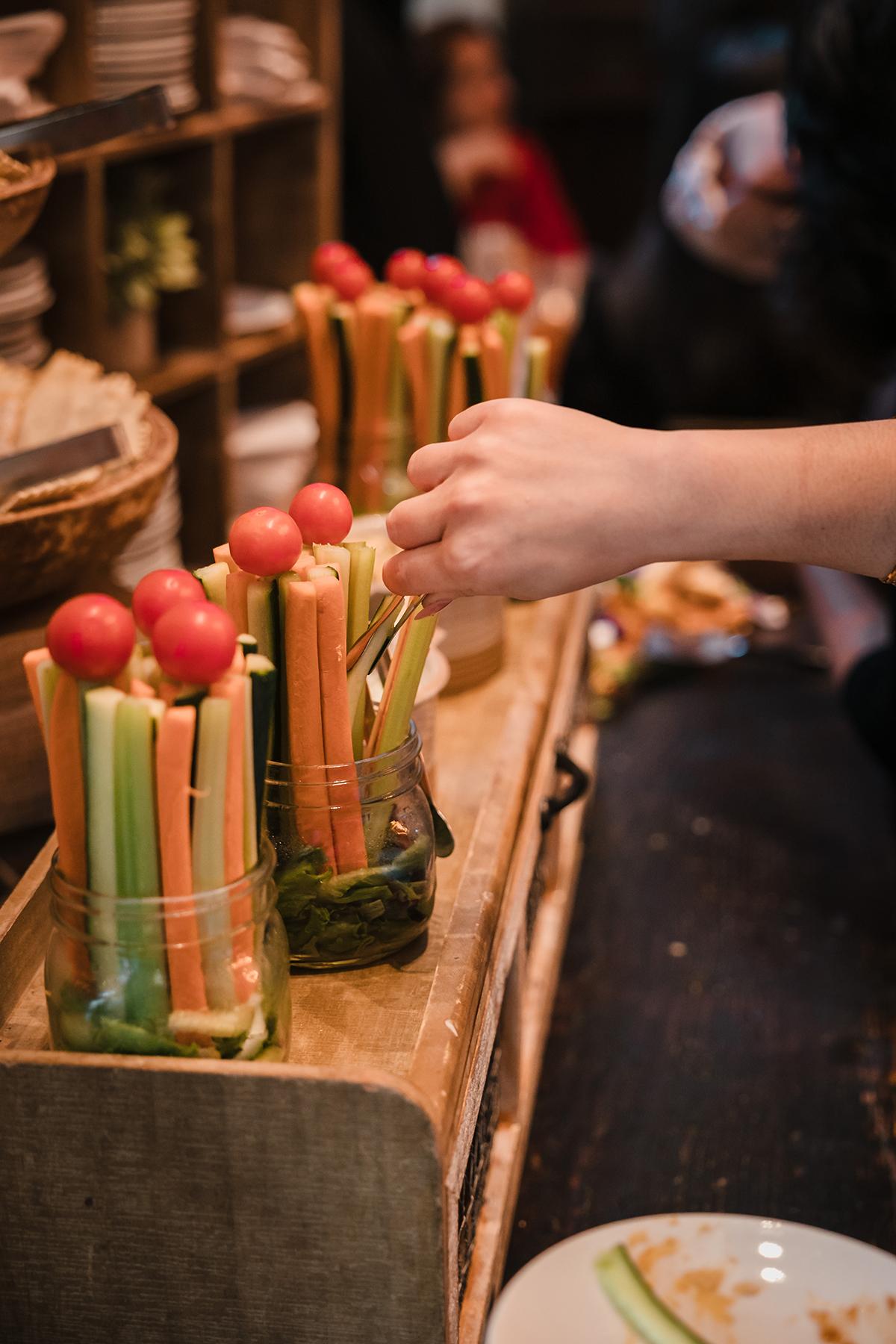 Jars filled with celery, carrot sticks, and cherry tomatoes; hand reaching for vegetables.