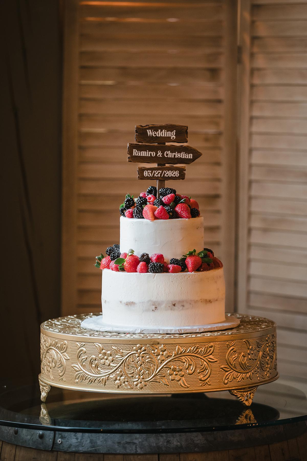 Two-tier white wedding cake with berries on gold stand.