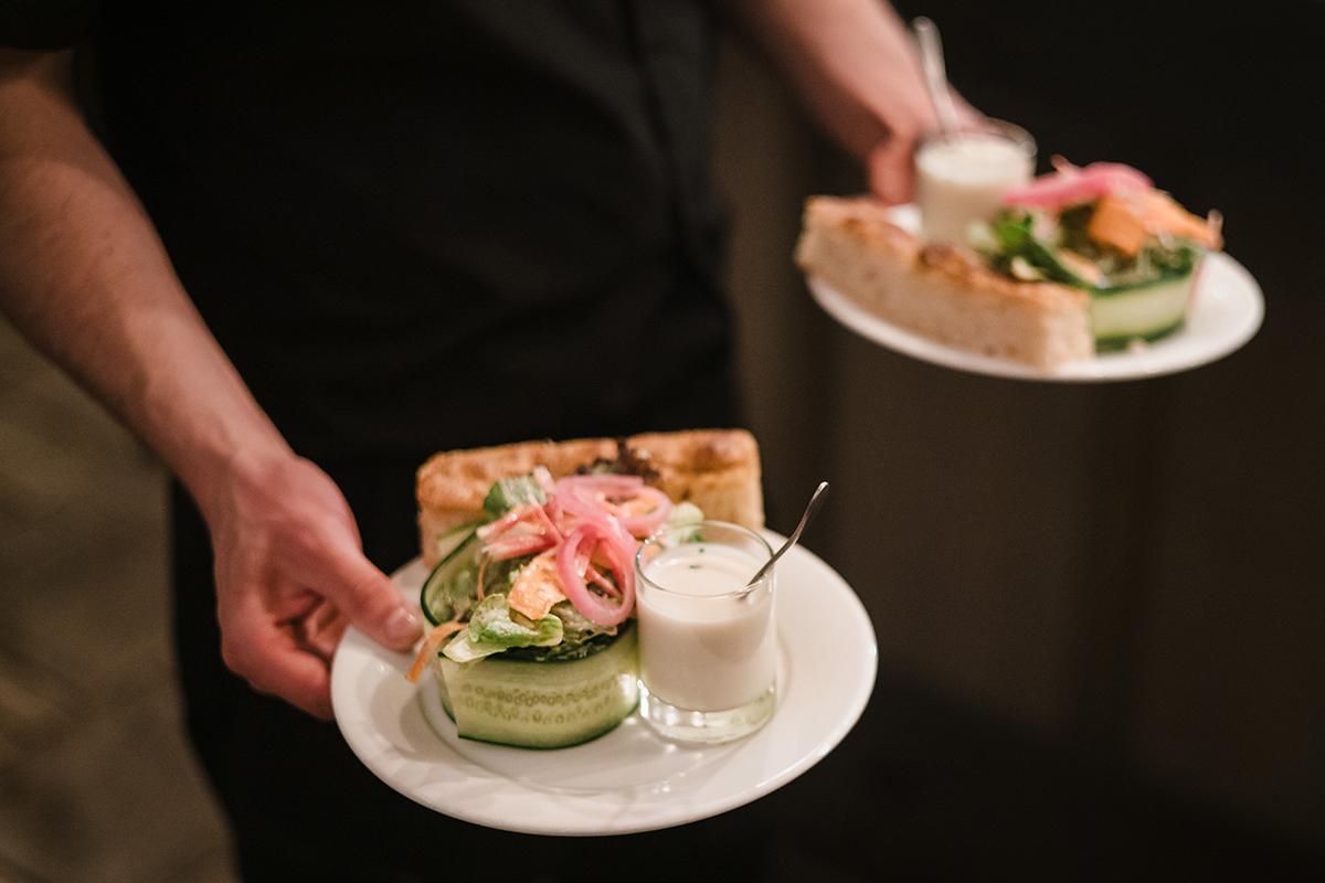 Server holding two plates with salads and small cream-filled glasses.