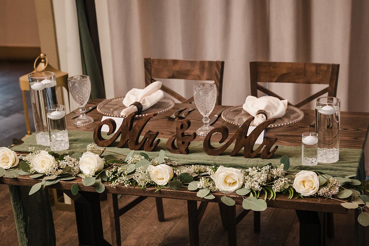Elegant table setting with "Mr &amp; Mr" sign, white roses, and glassware.