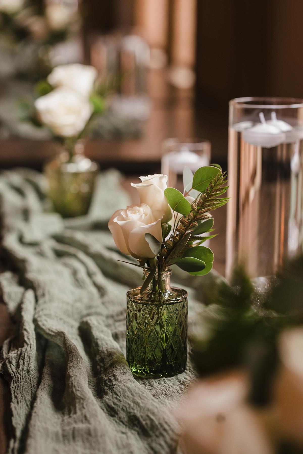 White roses in small green vases on a rustic table with soft lighting.