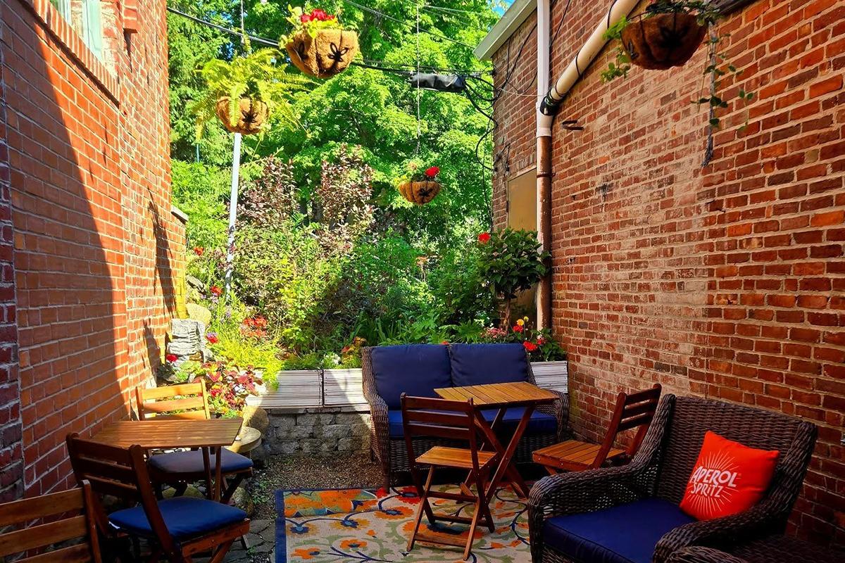 Cozy brick patio with blue chairs, tables, and hanging plants.