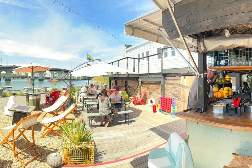 Outdoor café by the beach with seating and a bar under sunny skies.