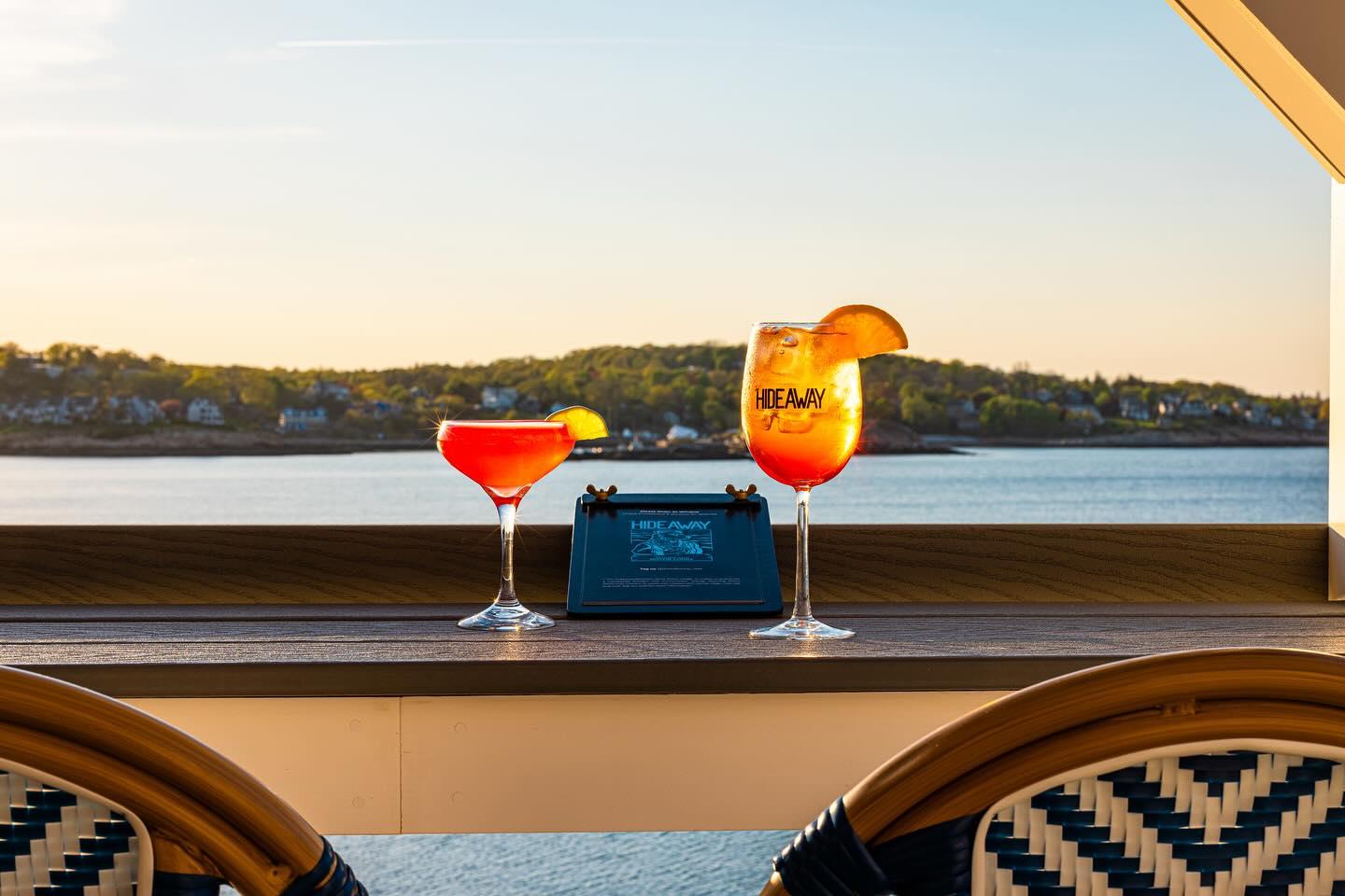 Two cocktails on a balcony overlooking a serene lake at sunset.