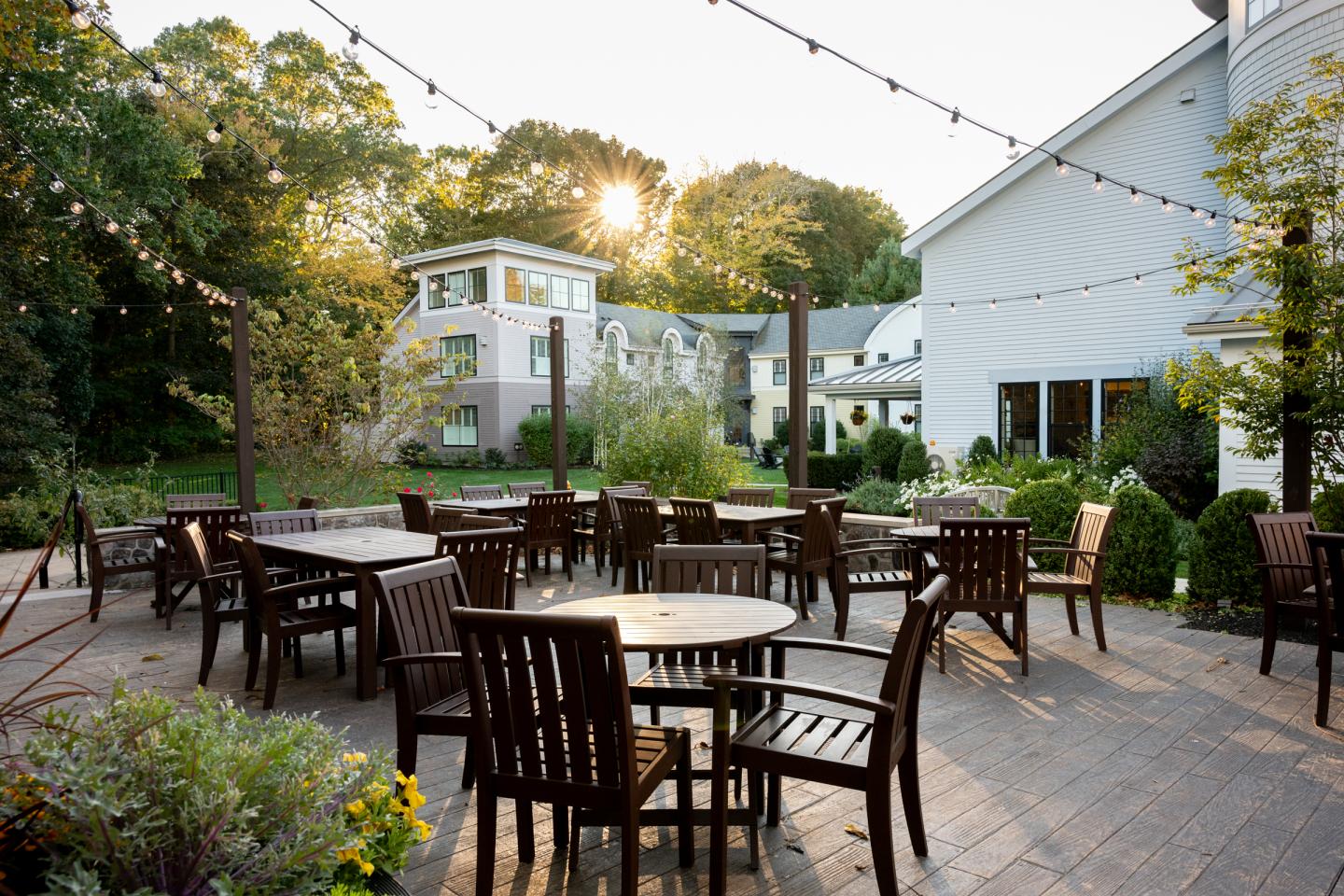 Outdoor patio with wooden tables and chairs, surrounded by greenery at sunset.