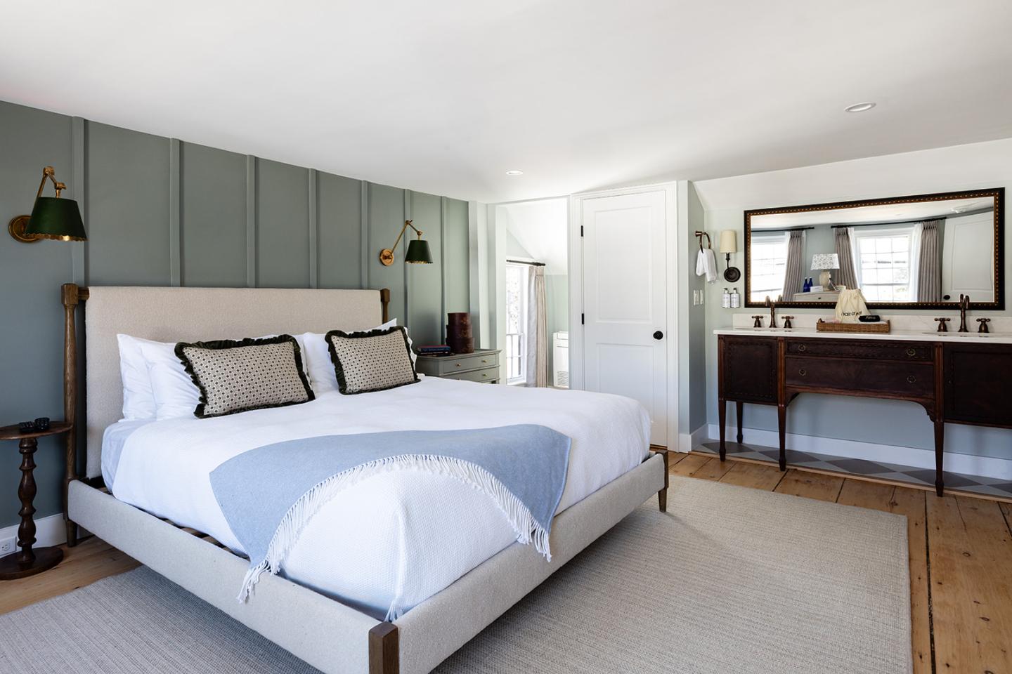Bright modern bedroom with white bed, green paneled wall, desk, and large mirror.