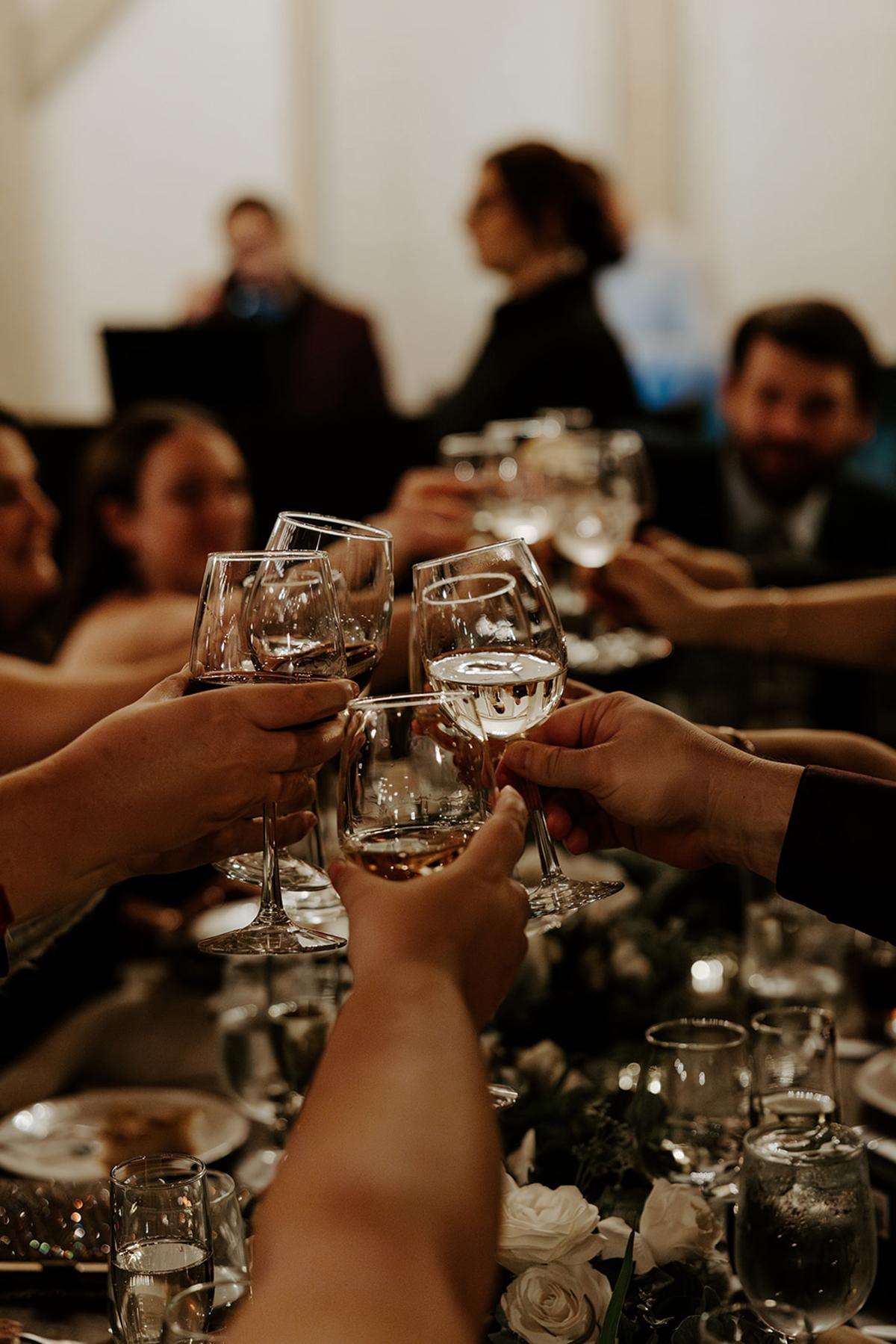 Friends clink wine glasses over a dinner table at a cozy gathering.