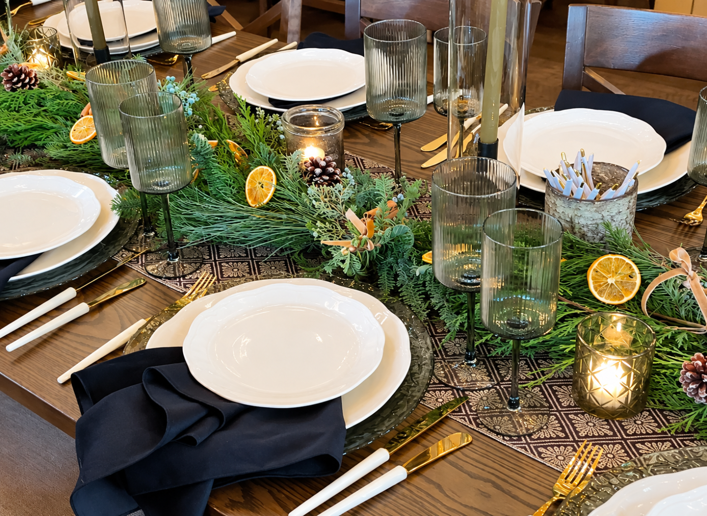 Festive dining table with greenery, candles, oranges, and place settings