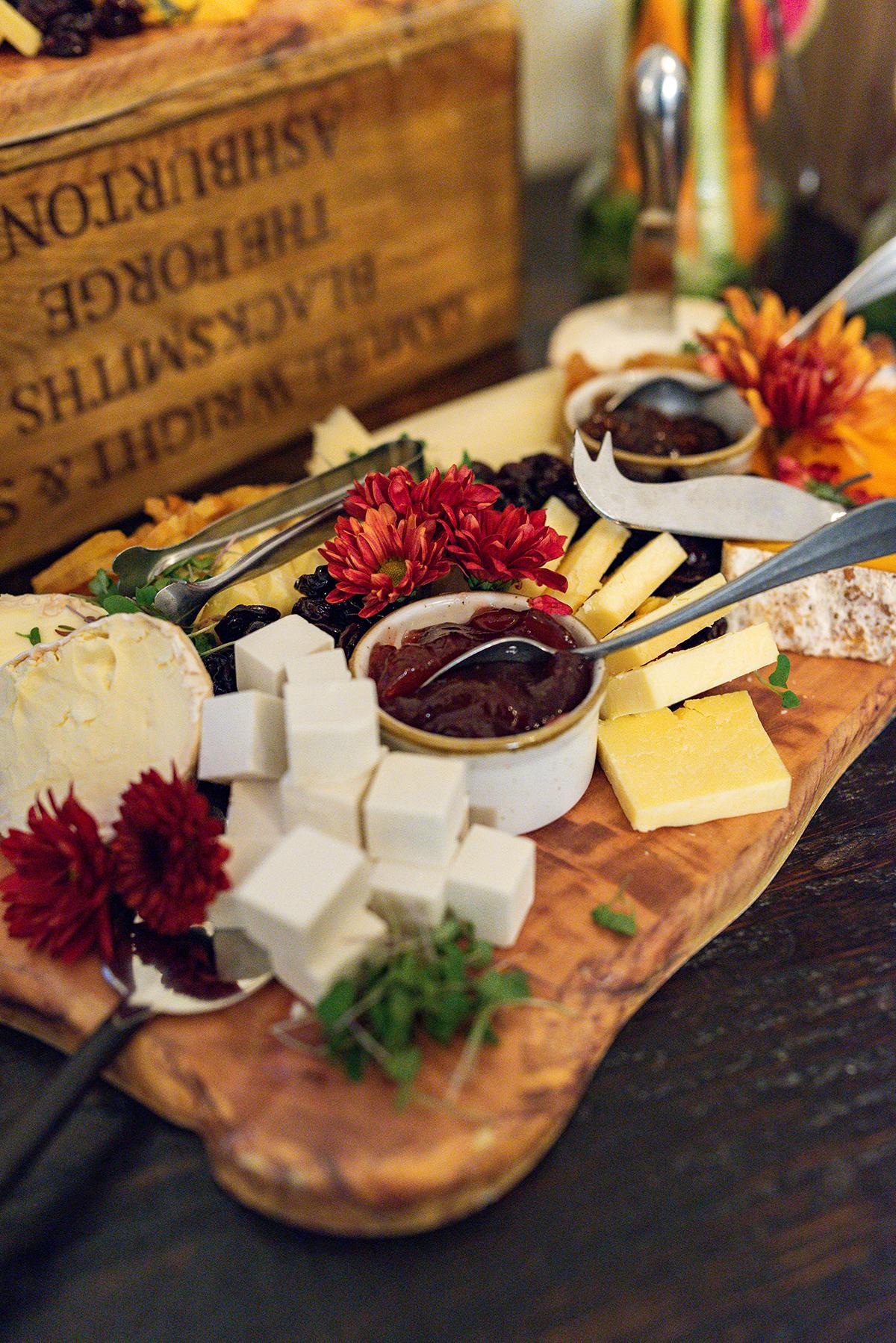 Rustic charcuterie board with cheeses, crackers, fruit, and flowers.