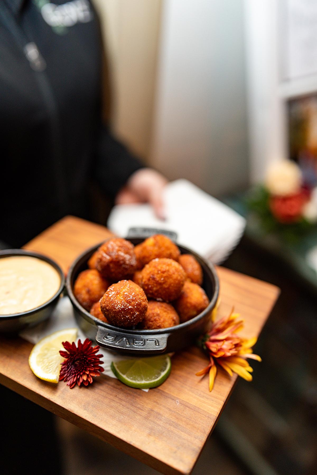 Bowl of fried cheese balls with dipping sauce on a wooden board.