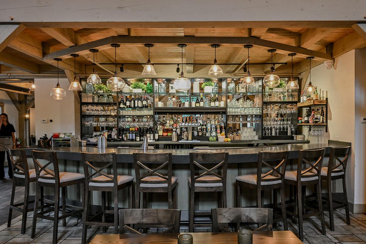 Rustic bar interior with wooden beams, high stools, and shelves of bottles