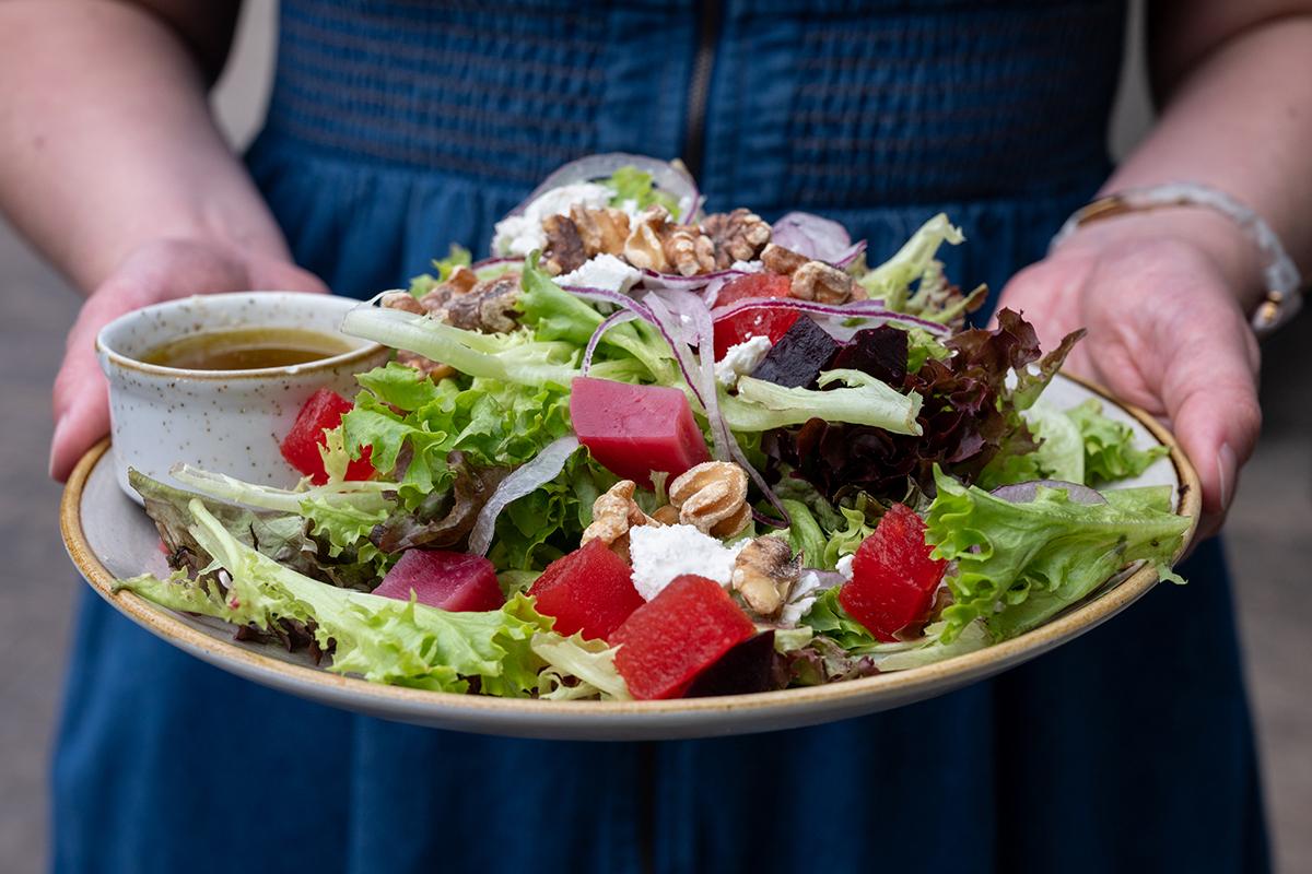 Person holding a colorful mixed salad with greens, strawberries, nuts, and cheese