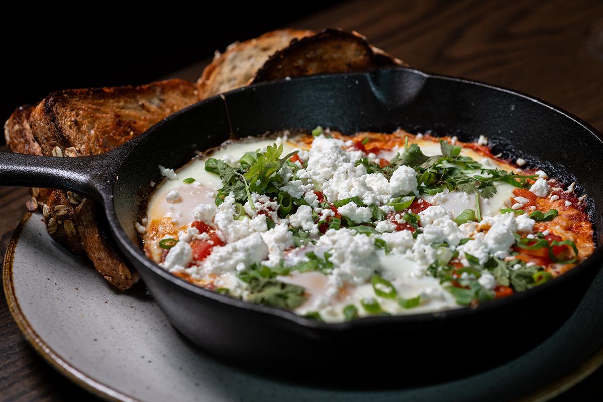 Skillet of baked eggs with tomato sauce, melted cheese, herbs, and bread