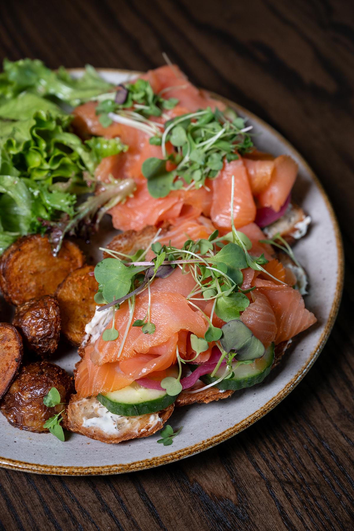 Bowl of roasted potatoes, smoked salmon, greens, and microgreens on a dark wood table