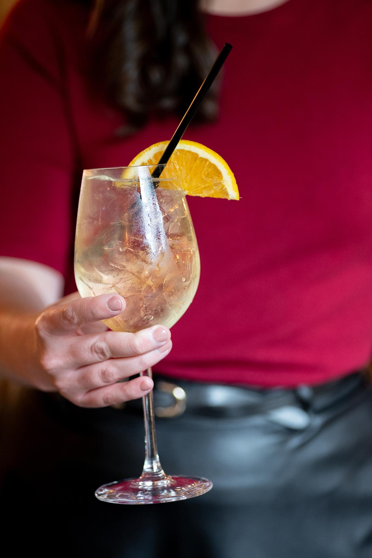 Woman holding a cocktail glass with ice, lemon slice, and black straw.