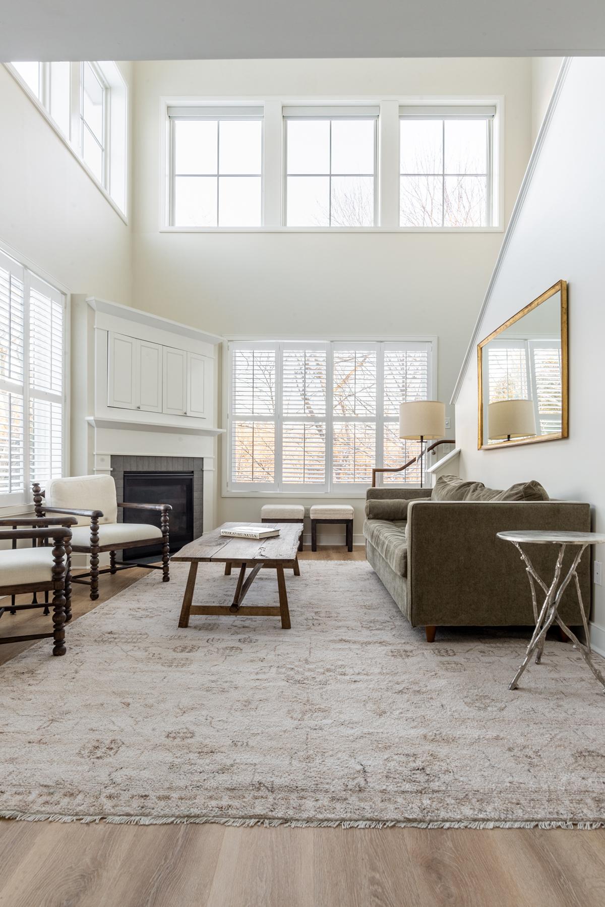 Bright living room with high windows, fireplace, sofa, and patterned rug