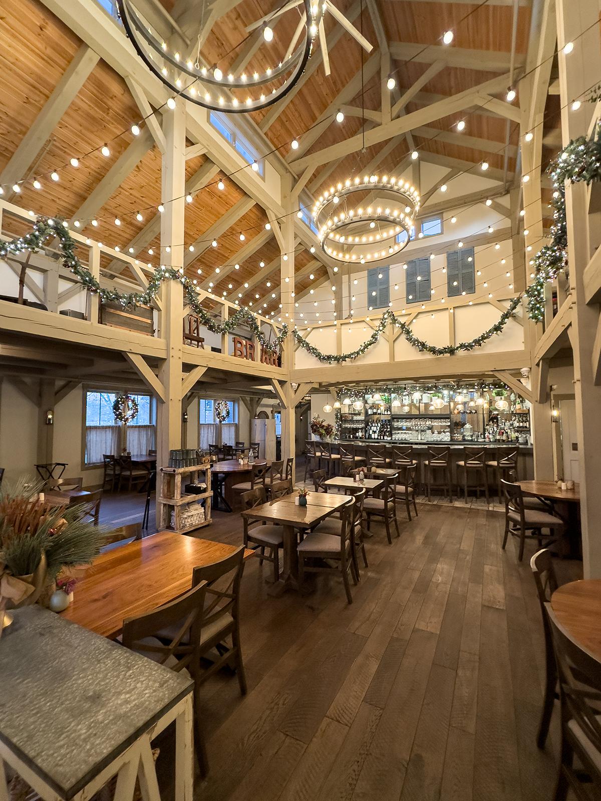 Warmly lit restaurant interior with wooden tables, exposed beams, and hanging chandeliers.