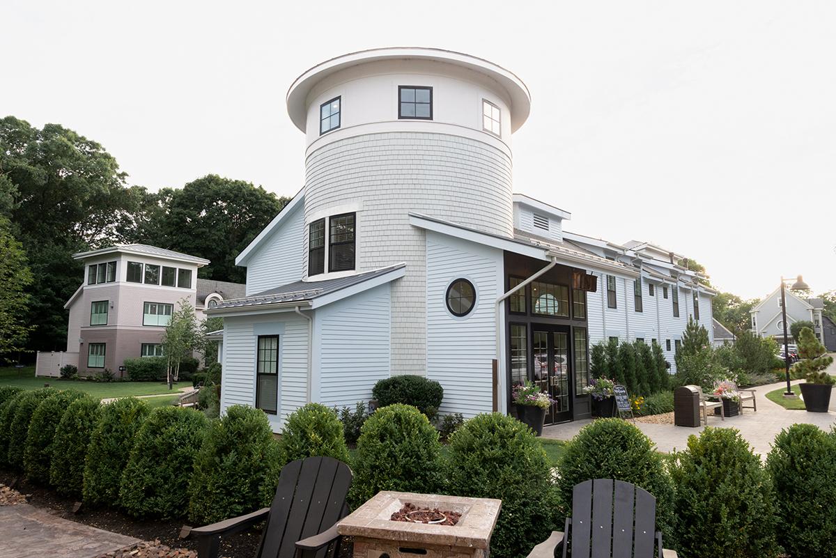 White round tower house with a porch, hedges, and Adirondack chairs.