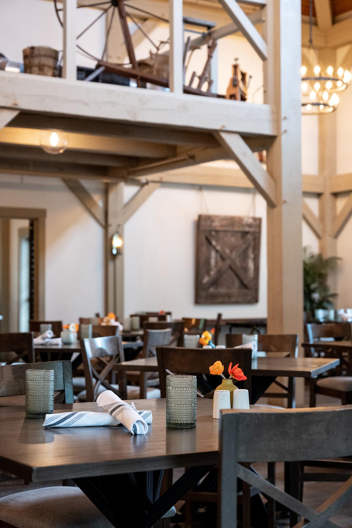 Warm, rustic restaurant interior with wooden beams, tables, and hanging lights.