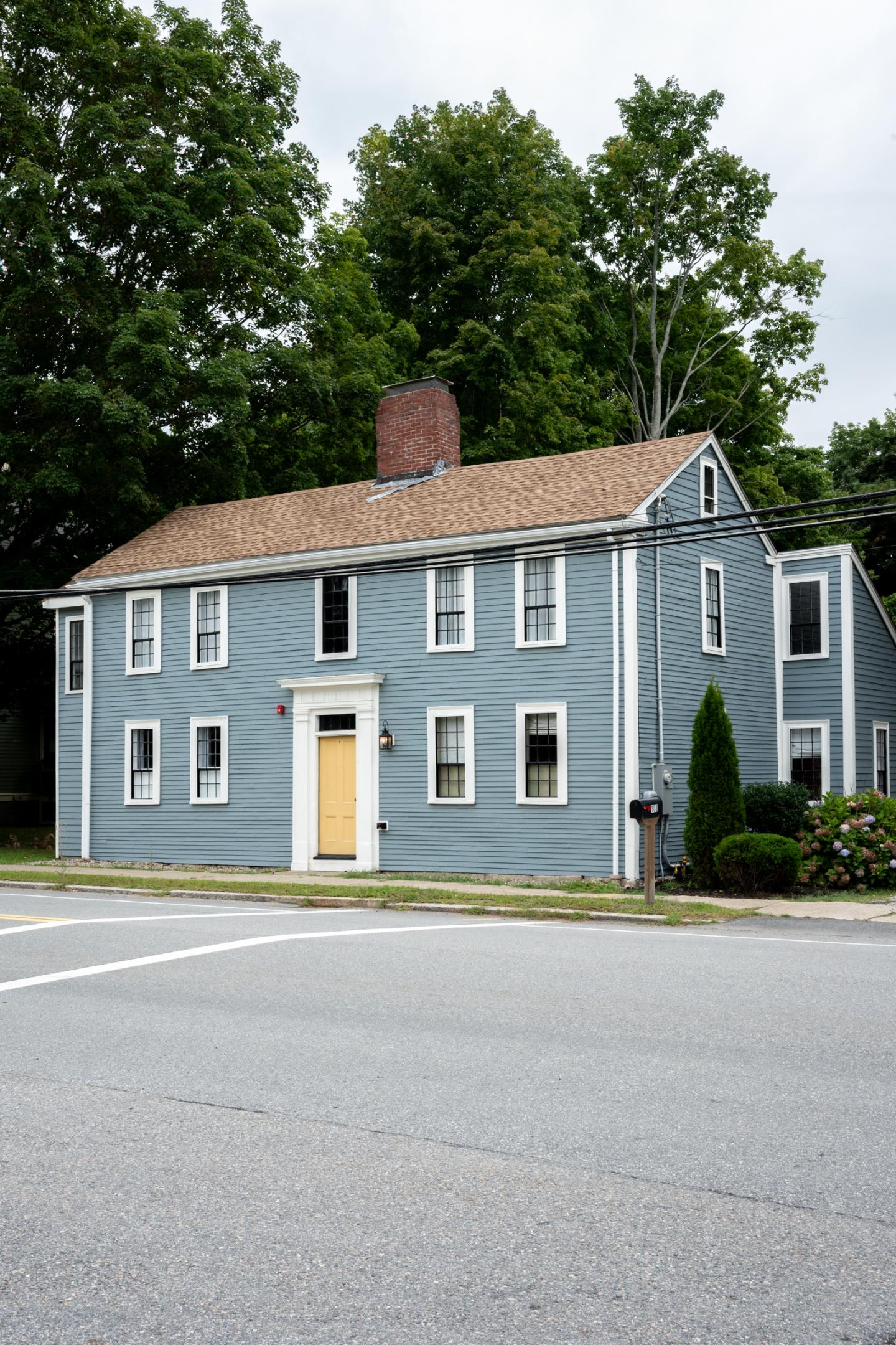 Gray-blue two-story house with white trim beside a quiet road.