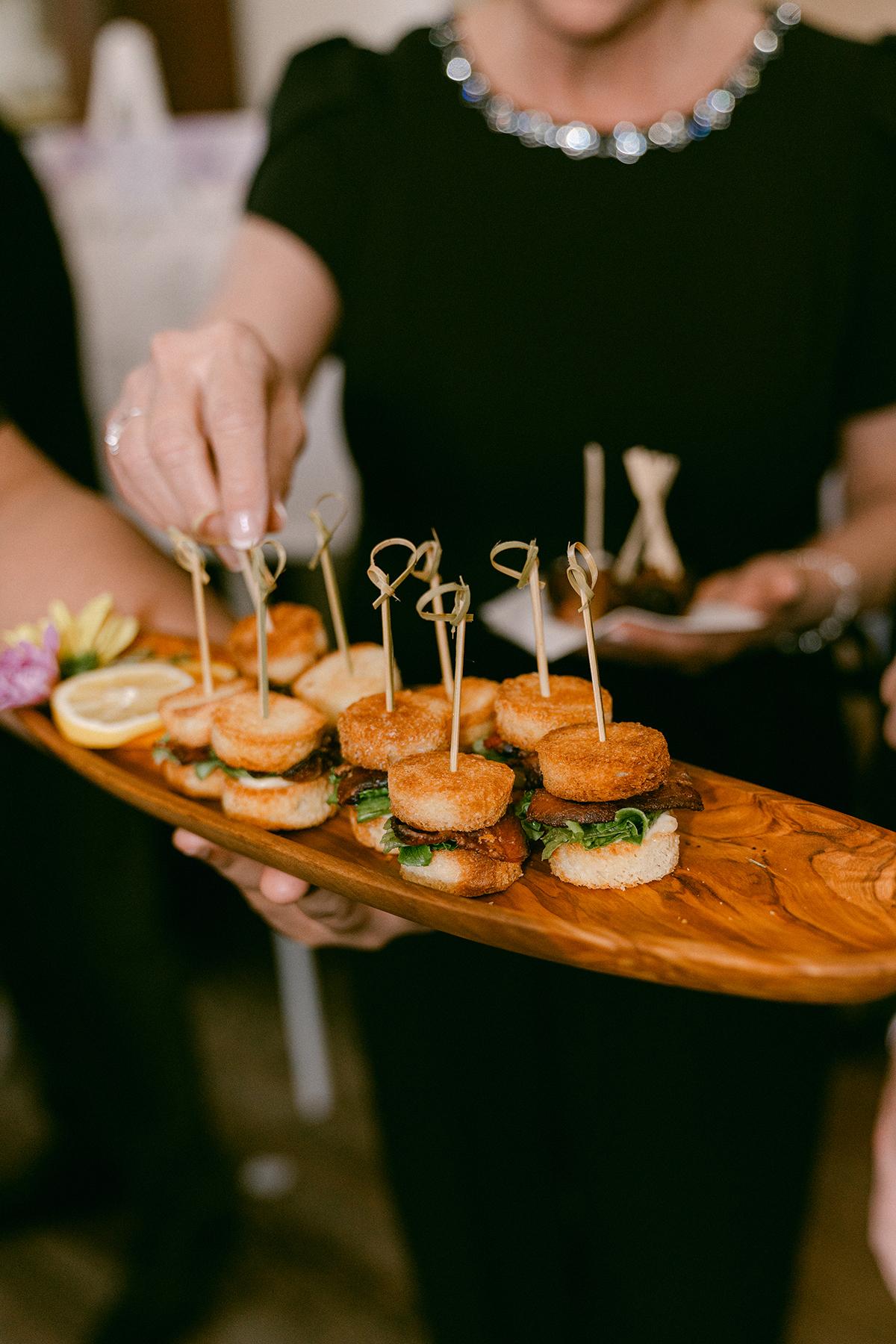 Woman serving bite-sized appetizers on a wooden board at a party.