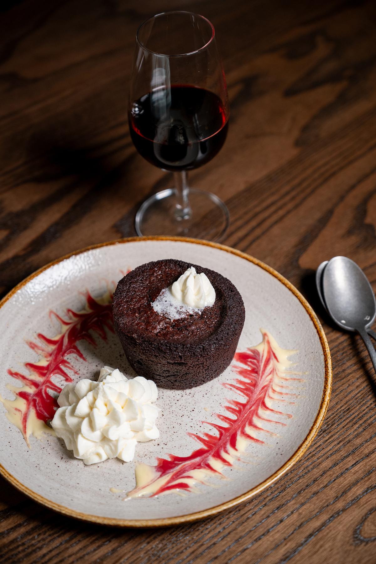 Chocolate lava cake with whipped cream and red berry sauce, beside red wine.