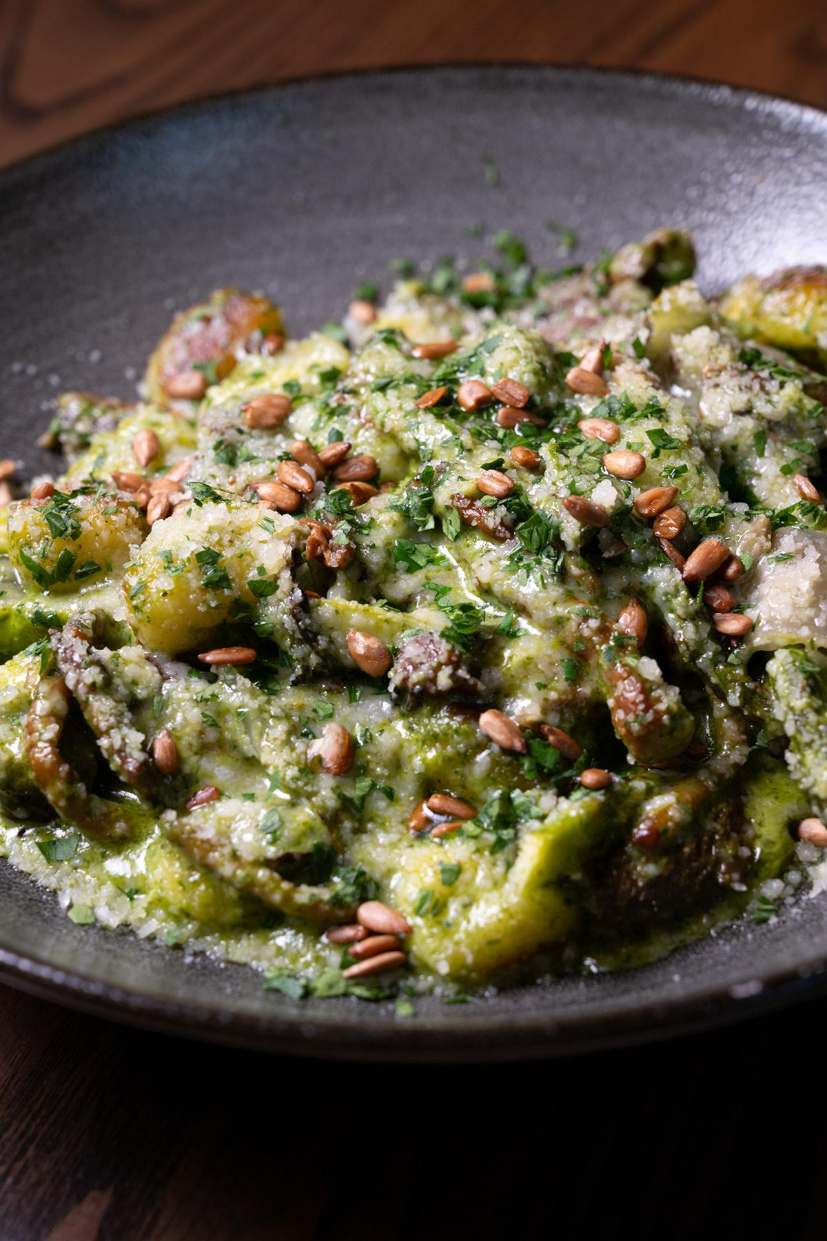Roasted green vegetables with herbs, cheese, and breadcrumbs in a dark bowl.