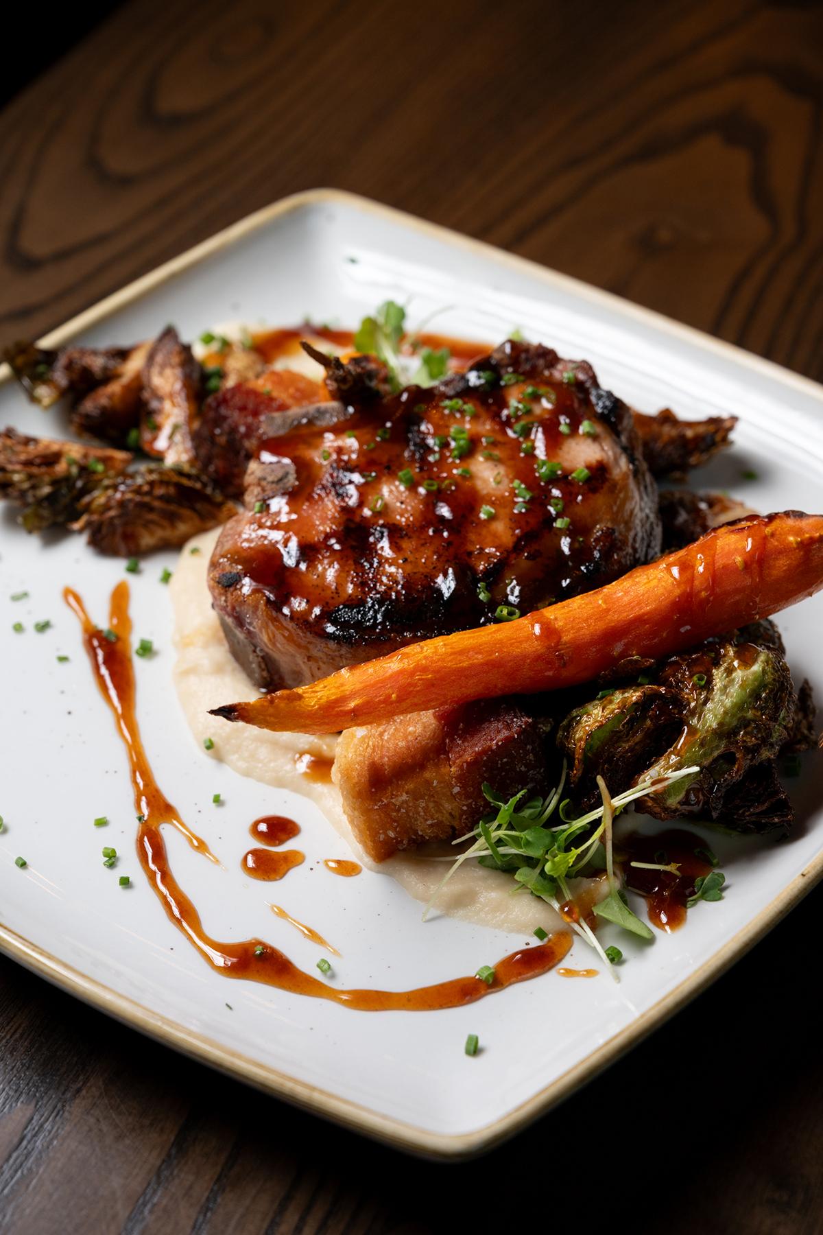 Glazed grilled meat with carrots and greens on a white square plate.