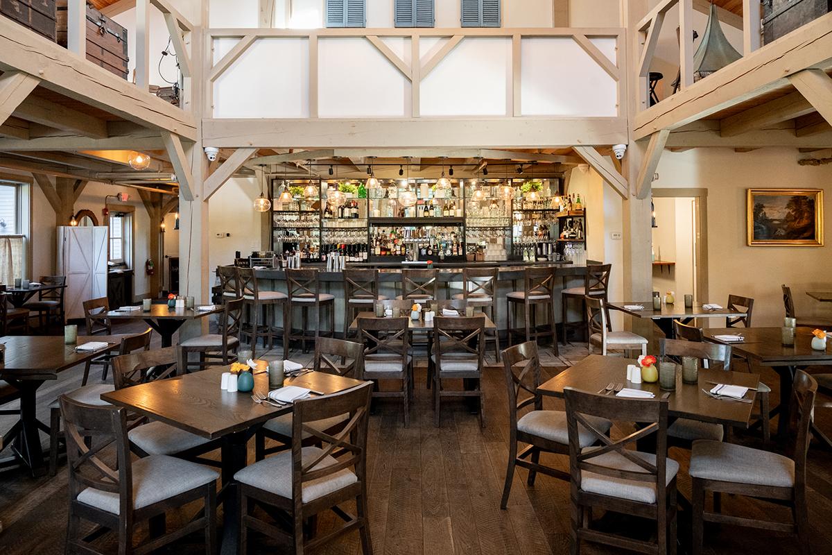 Warm, wood-beamed restaurant dining room with set tables and a bar at the back.