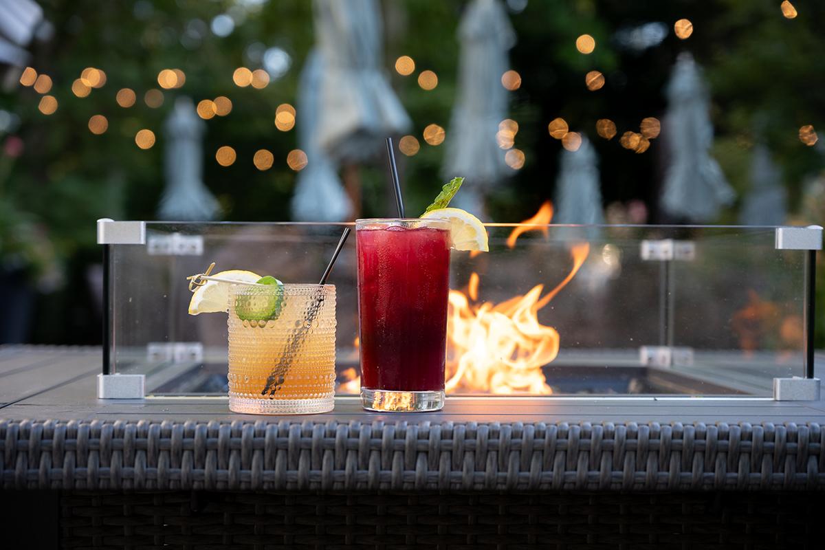 Three colorful cocktails on a bar with warm string lights in the background.