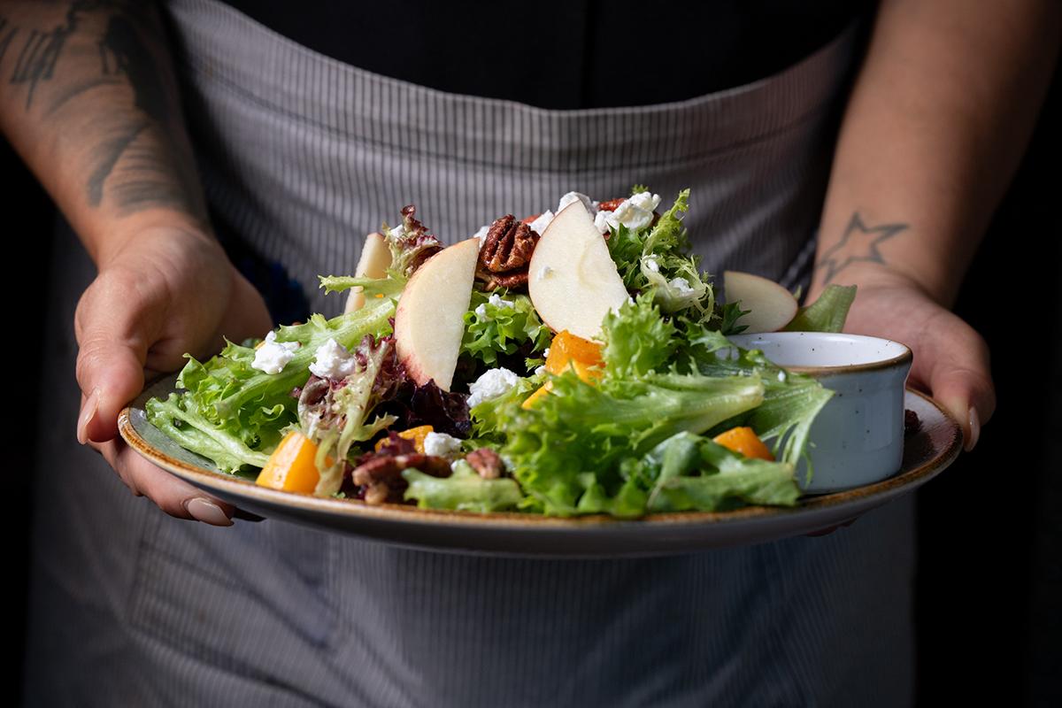 Person holding a plate of fresh mixed salad with greens, mushrooms, and edible flowers.