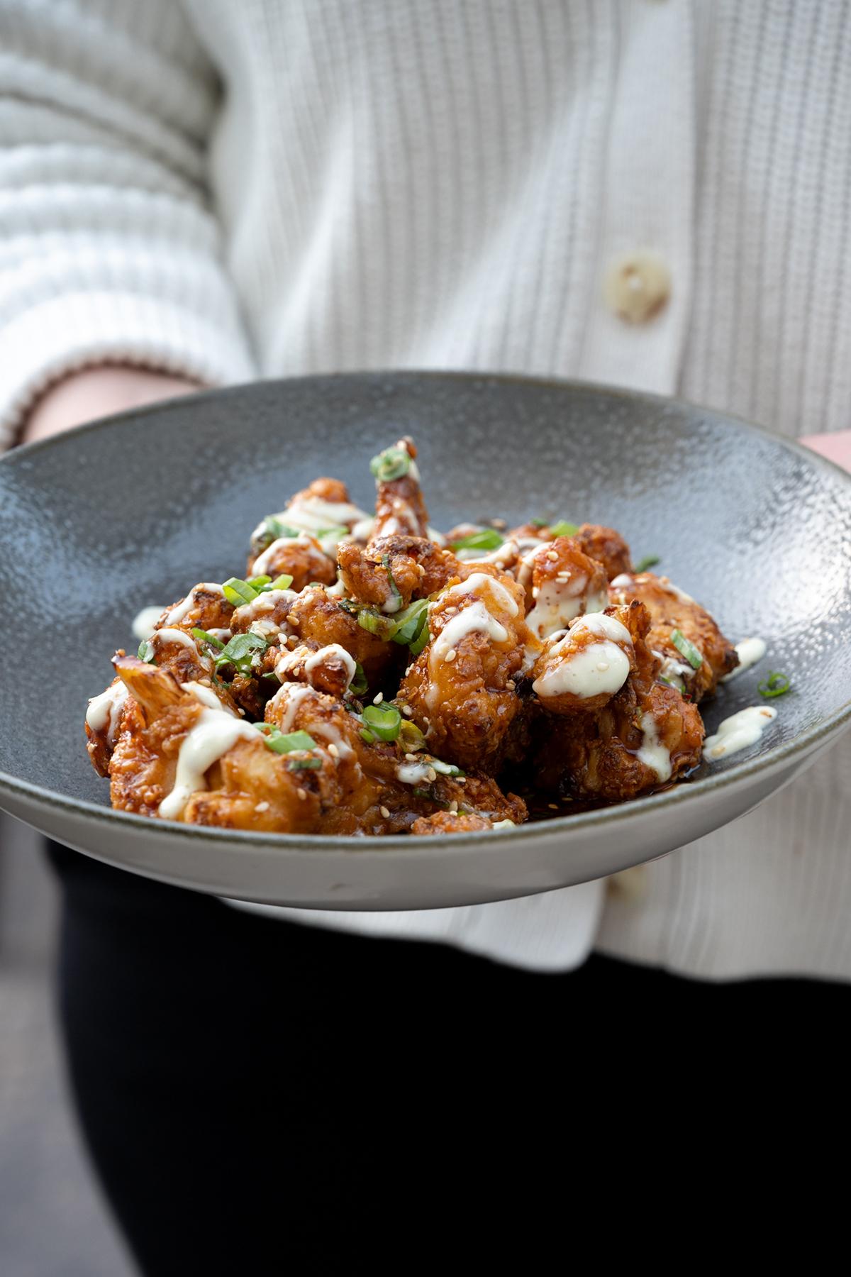 Bowl of saucy fried chicken bites topped with herbs and cheese.